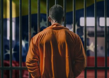 hombre tras las rejas de una celda de prision con bandera de Venezuela en el fondo