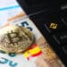 moneda de bitcoin sobre billetes de euros junto a calculadora con logo de bitcoin