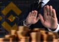 persona rechazando monedas apiladas con plataforma y logo de binance en el fondo