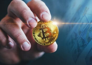 mano sostiene moneda de bitcoin con billetes de dolares en cuerda