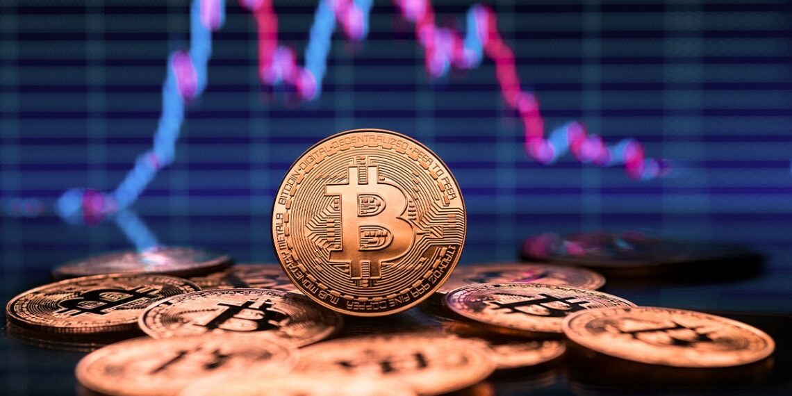 moneda de bitcoi entre otras monedas de bitcoin disperzadas sobre mesa con gráfico de precio bajista en el fondo