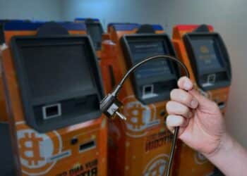 mano sostiene cable de poder desconectado con cajeros automaticos de bitcoin apagados en el fondo