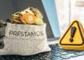 monedas de diversas criptomonedas en bolsa para prestamos sobre computadora junto a icono de advertencia