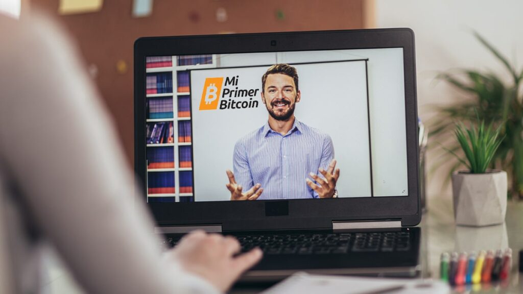 persona viendo clase online en pantalla de computadora con logo de Mi Primer Bitcoin en pizarra