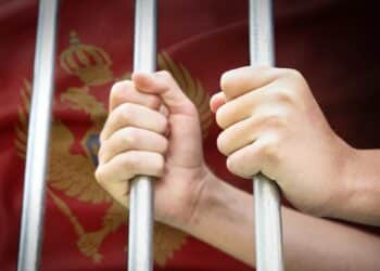 manos sujetando barrotes de prision con bandera de Montenergo en el fondo