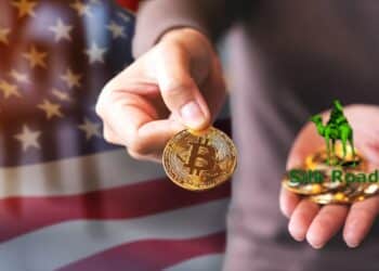 persona ofreciendo moneda de bitcoin con logo de Silg Road sobre monedas de bitcoin apiladas en su mano con bandera de Estados Unidos en el fondo