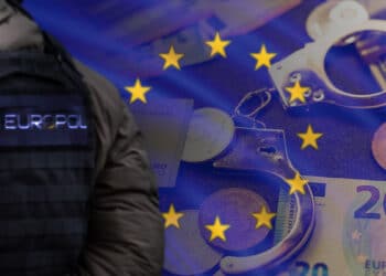 Policía con chaleco de la EUROPOL con esposas monedas de bitcoin y ethereum y billetes de euro en el fondo con bandera de europa superpuesta