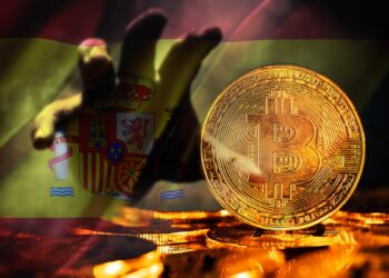 mano sombria acercandose a moneda de bitcoin con bandera de españa en el fondo