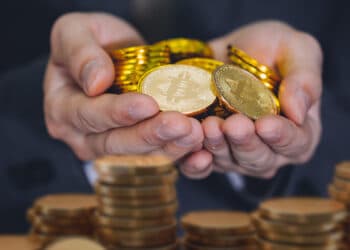 manos sosteniendo monedas de bitcoin detras de monedas apiladas