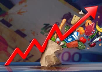 bolsa de compras golpeada por flecha creciente con billetes de pesos argentinos en el fondo y bandera de Argentina reflejada sobre mesa
