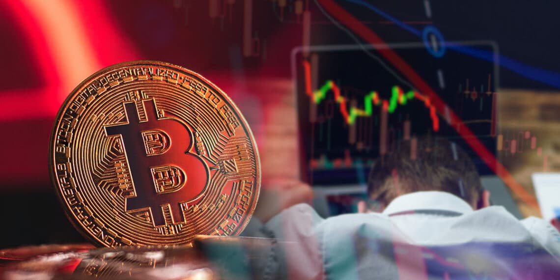 moneda de bitcoin en rojo junto a trader arrepentido frente a computadora con grafico bajista de precio en pantalla y velas de precio superpuestas.