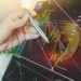 mao de trader sosteniendo boligrafo sobre pantalla, señalando bajada en grafico de precio con moneda de bitcoin en el fondo
