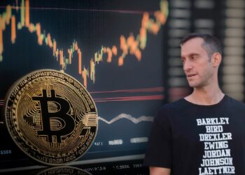 Soctt Melker observando moneda de bitcoin apoyada en pantalla con grafico de precio
