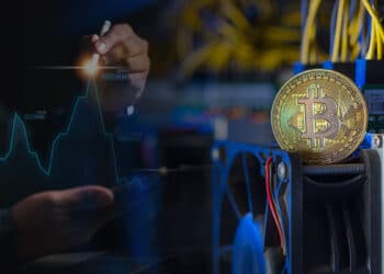 moneda de bitcoin sobre mienro ASIC de criptmonedas junto a persona señalando máximo en grafico de linea