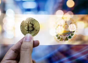 mano sostiene moneda de bitcoin con bandera de El Salvador en el fondo