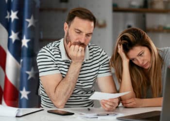 pareja preocupada observando cheque con bandera de Estados Unidos en el fondo