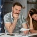 pareja preocupada observando cheque con bandera de Estados Unidos en el fondo