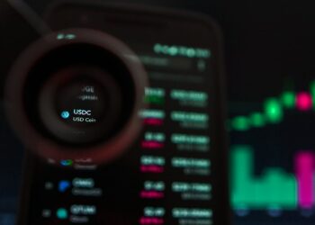 lupa sobre pantalla de telefono movil enfocando USDC con graficos de precio en el fondo