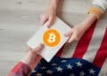 una manos sosteniendo un documento en el que se observa el logo de bitcoin y de fondo la bandera de Estados Unidos.