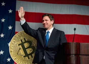 Ron de Santis en campaña política con moneda de bitcoin detrás