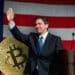 Ron de Santis en campaña política con moneda de bitcoin detrás