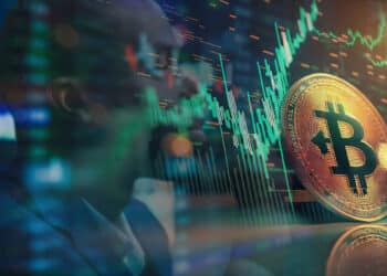 moneda de bitcoin con grafico de precio en pantalla junto a analista de precio detrás de pantalla en el fondo