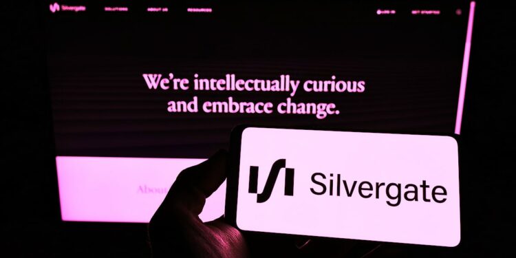 mano sosteniendo telefono movil con aplicación de silvergate en pantalla y página web en el fondo