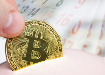 mano insertando moneda de bitcoin en alcancía con calendario pasando paginas en el fondo