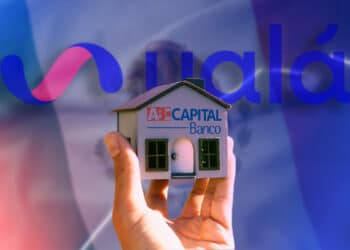 mano sostiene modelo de casa con logo de ABC Capital banco con banderas de México y logo de Ualá en el fondo