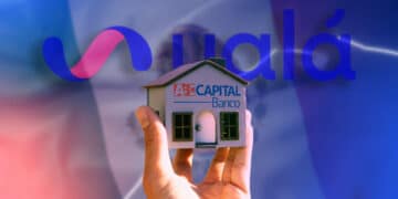 mano sostiene modelo de casa con logo de ABC Capital banco con banderas de México y logo de Ualá en el fondo