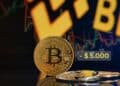 moneda de bitcoin junto a ventala señalando 5.000 dólares menos de precio con grafico de precio y logo de Binance en pantalla al fondo