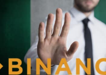 hombre haciendo señal de pare con la mano a logo de binance con bandera de Nigeria en el fondo