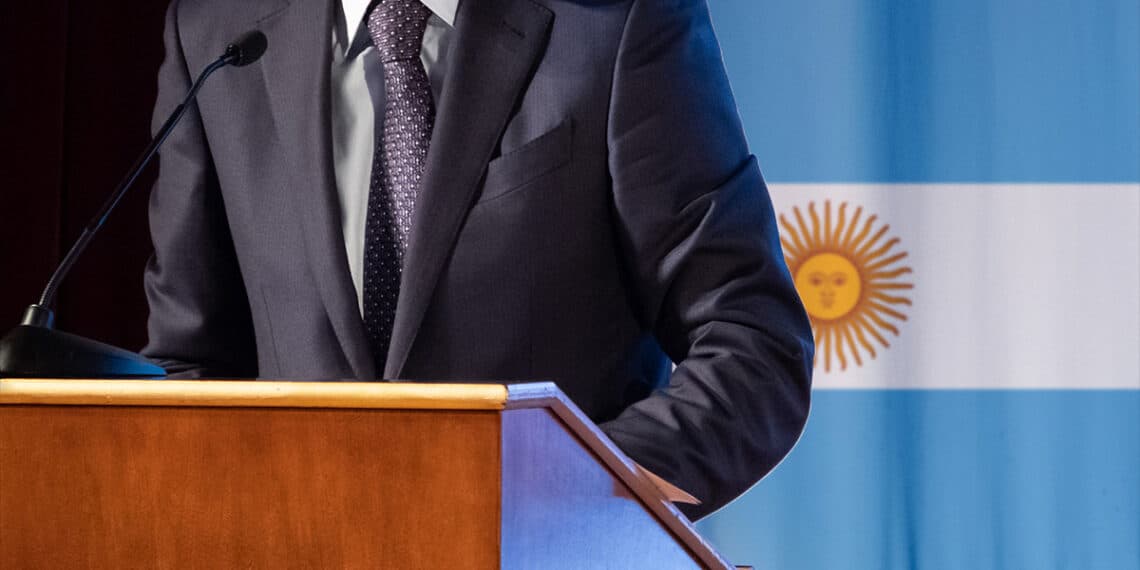 hombre dando discurso con bandera de Argentina en el fondo