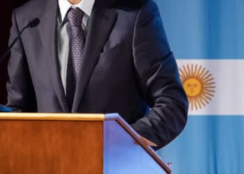 hombre dando discurso con bandera de Argentina en el fondo