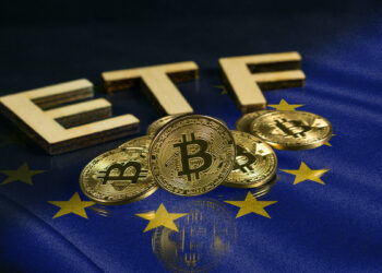 monedas de bitcoin junto a letras formando ETF sobre mesa de cristal reflejando bandera de Europa