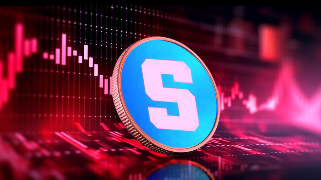moneda del token SAND de The Sandbox sobre superficie con graficos de precio en rojo