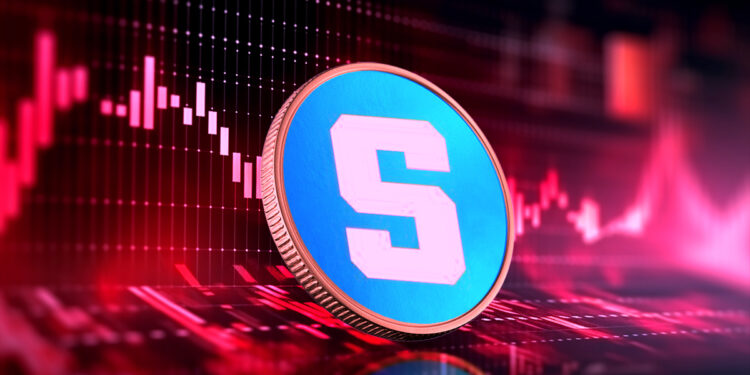 moneda del token SAND de The Sandbox sobre superficie con graficos de precio en rojo