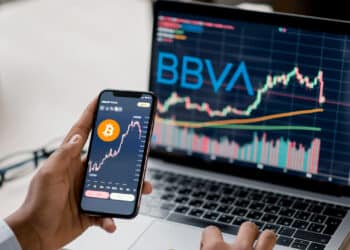 Celular y computadora con precio de bitcoin y logo de BBVA.