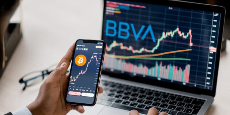 Celular y computadora con precio de bitcoin y logo de BBVA.