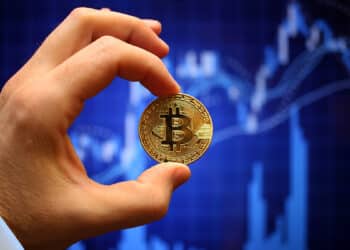 mano sosteniendo moneda de bitcoin con grafico de precio alcista en el fondo