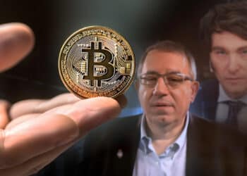 mano sosteniendo moneda de Bitcoin con Carlos Maslaton y Javier Milei en el fondo