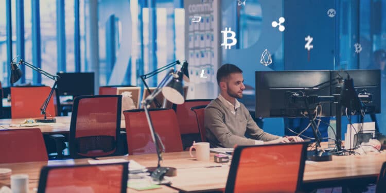 desarrollador sentado en escritorio de oficina vacía con logos de criptomonedas detrás