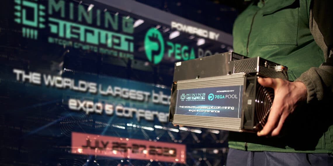 persona sosteniendo minero asic con anuncio digital de la Mining Disrupt conference 2023