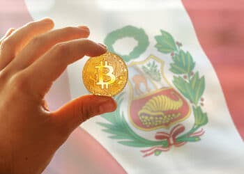 mano sosteniendo moneda de bitcoin con bandera de Perú en el fondo