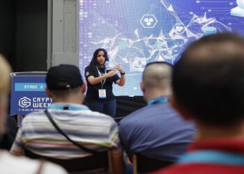 Mujer frente a un auditorio lleno dirigiendo al publico.