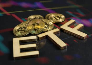 monedas de bitcoin junto a letras formando ETF sobre superficie de cristal con grafico de precio reflejado