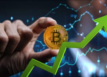 flecha señalando alza sobre mano sosteneindo moneda de bitcoin con graficos de precio digital en el fondo