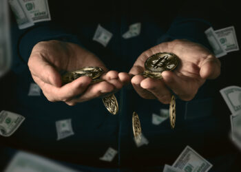 manos sosteniendo monedas de bitcoin rodeadas por billetes de dólares cayendo