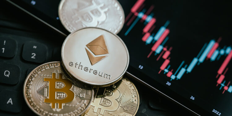 moneda de ethereum sobre monedas de bitcoin junto a pantalla con grafico de precio