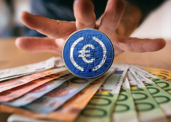 moneda de EURC sobre billetes de euto con mano detrás
